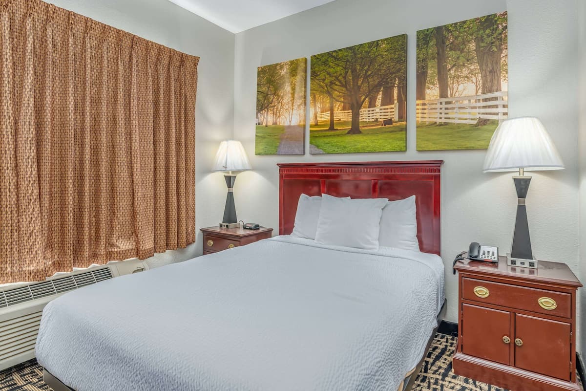 A hotel room with a large bed, two bedside tables, a red headboard, and three framed pictures on the wall.