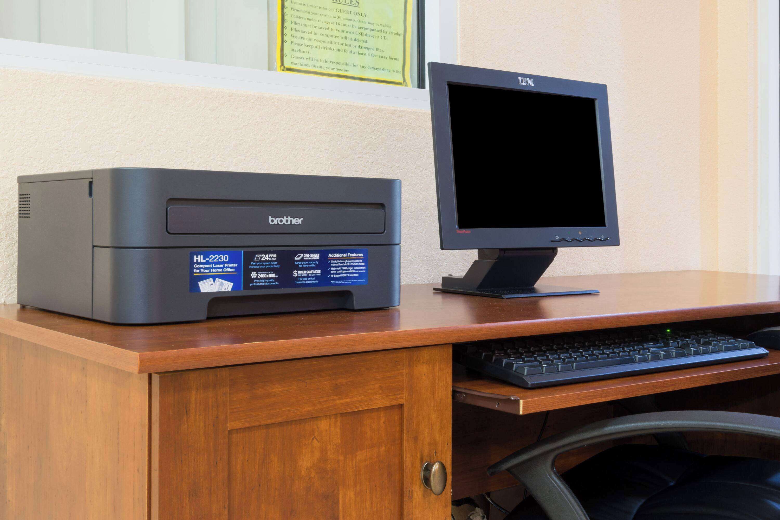 A Brother HL-2230 compact laser printer on a wooden desk with a keyboard and an IBM monitor.