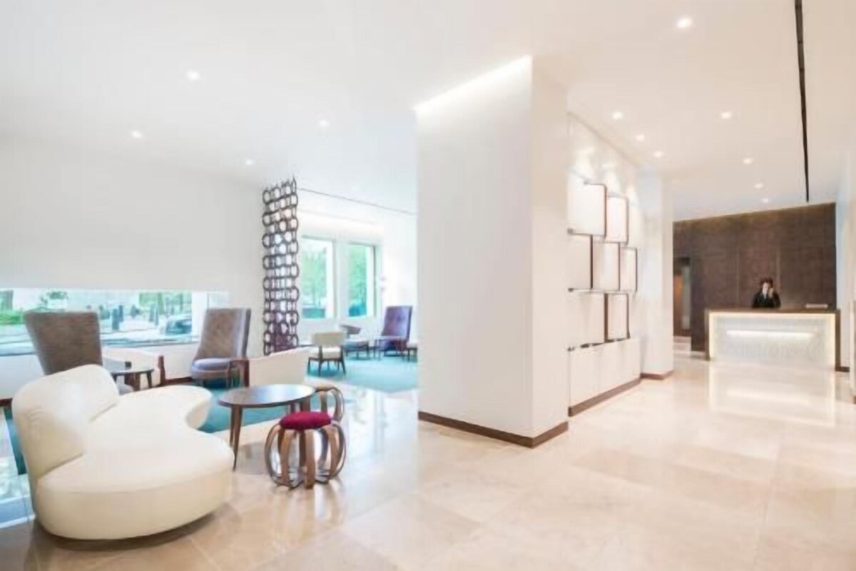 A modern hotel lobby with a reception desk, seating area, and a view of the outdoors.