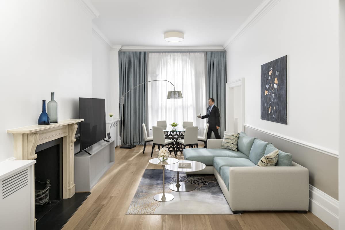 A modern living room with a fireplace, a sofa, a coffee table, and a dining area with a chandelier.