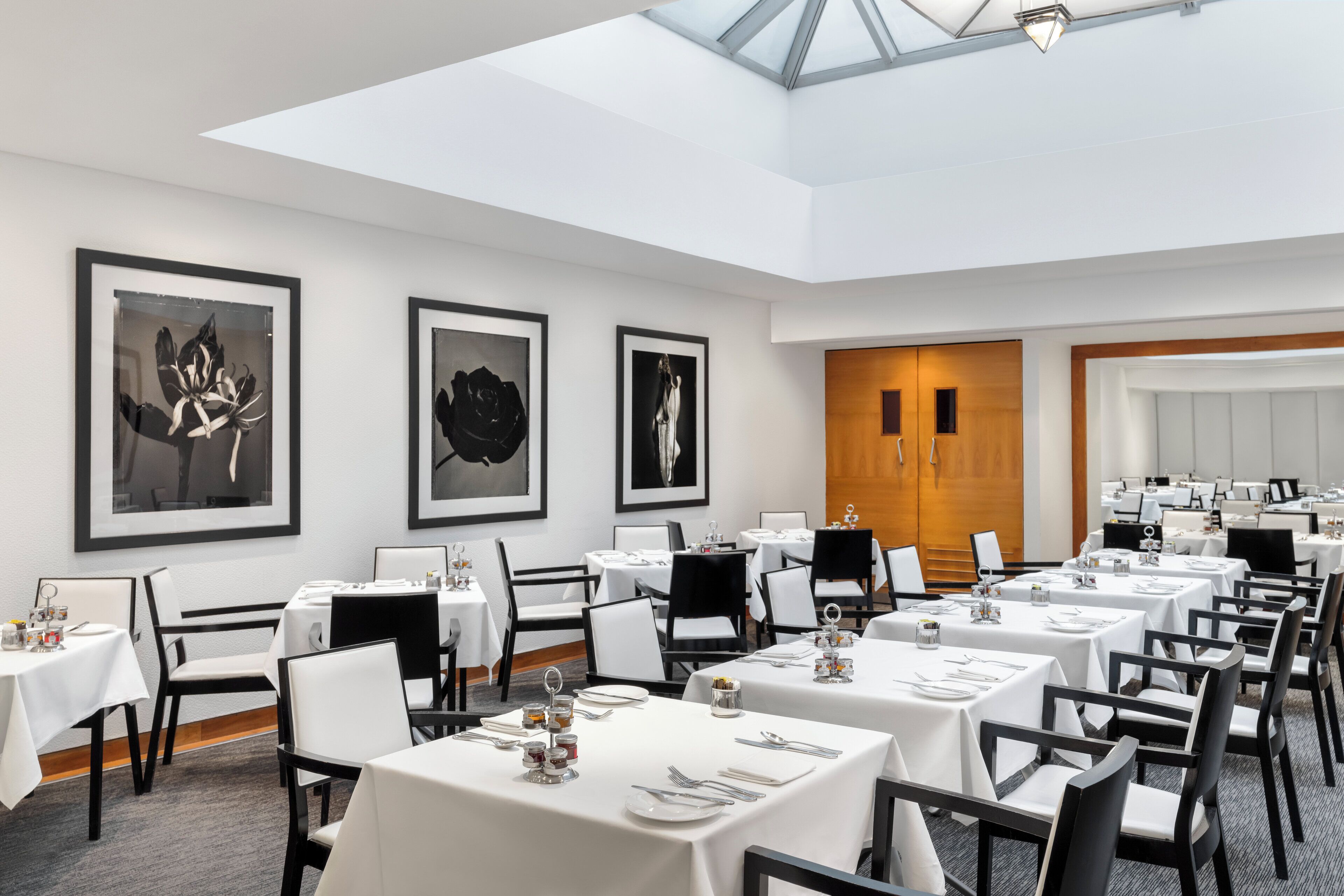 Comedor de hotel con mesas dispuestas para los huéspedes, obras de arte en las paredes y un tragaluz.
