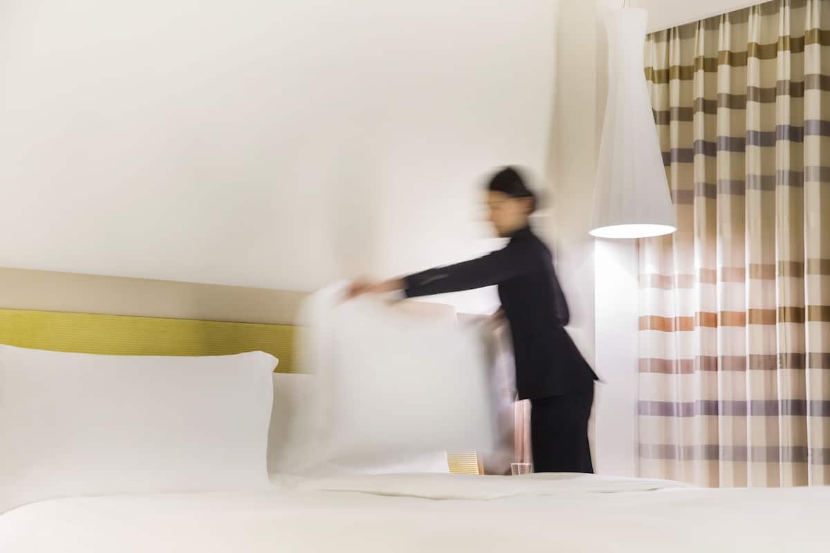 A hotel room with a bed, a headboard, a bedside table, and a window with curtains.