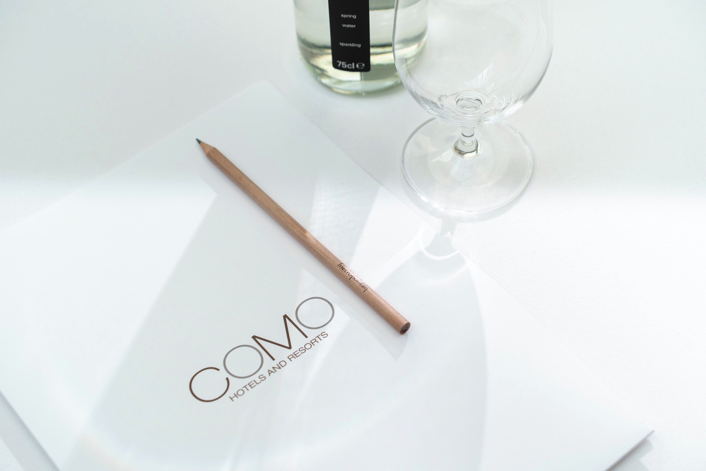 A clear glass bottle labeled "spring water" and a clear glass wine glass on a white surface.