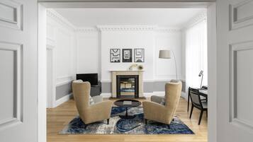 A room with two armchairs, a small round table, a fireplace, and framed artwork on the wall.