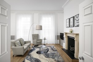 A modern living room with a sofa, armchair, coffee table, floor lamp, fireplace, and artwork on the wall.