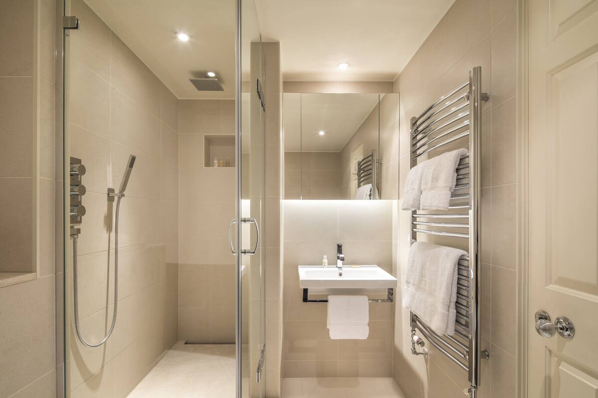 A modern bathroom with a glass shower enclosure, a white sink, and a towel rack.