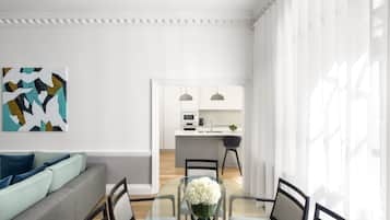 A modern living room with a glass dining table, a sofa with cushions, and a kitchen in the background.