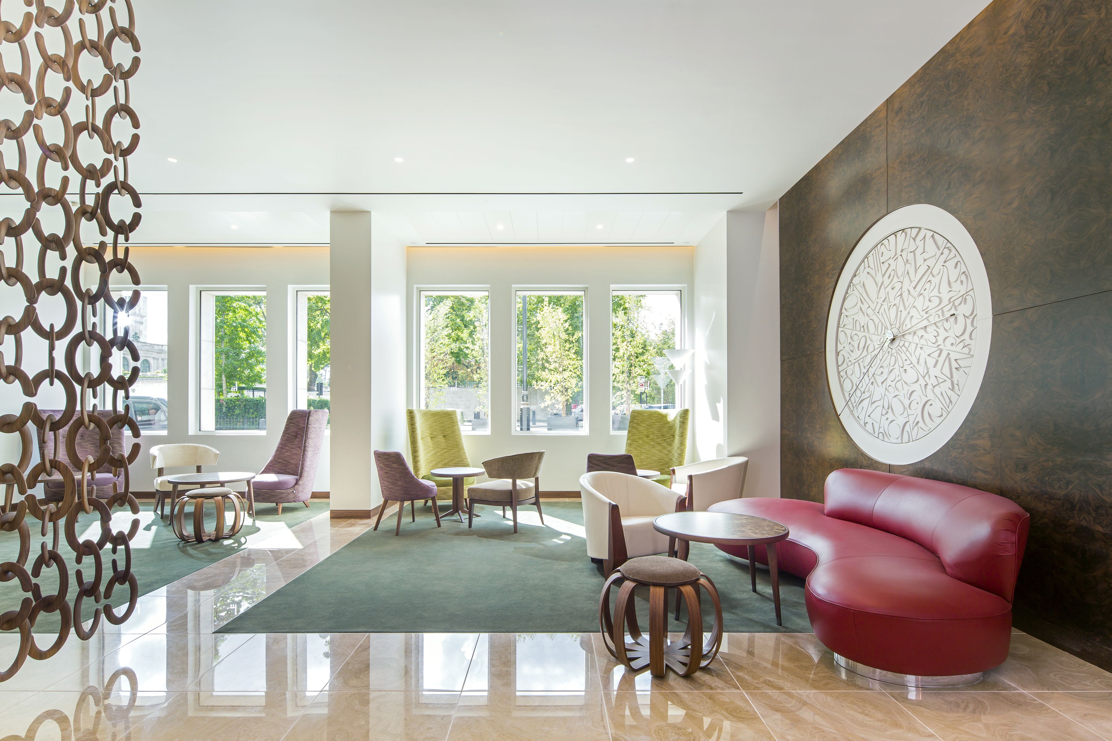 A modern lobby with a red sofa, multiple chairs, a round table, and large windows with a view of trees.