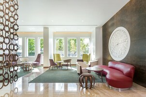 A modern lobby with a red sofa, multiple chairs, a round table, and large windows with a view of trees.