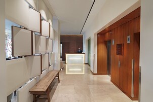 A modern hallway with a wooden bench, a reception desk, and an elevator.