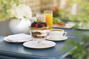 Ein Dessert in einer Glaskugel auf einem Tisch mit einem weißen Teller, einer Tasse Kaffee und einem Glas Orangensaft.