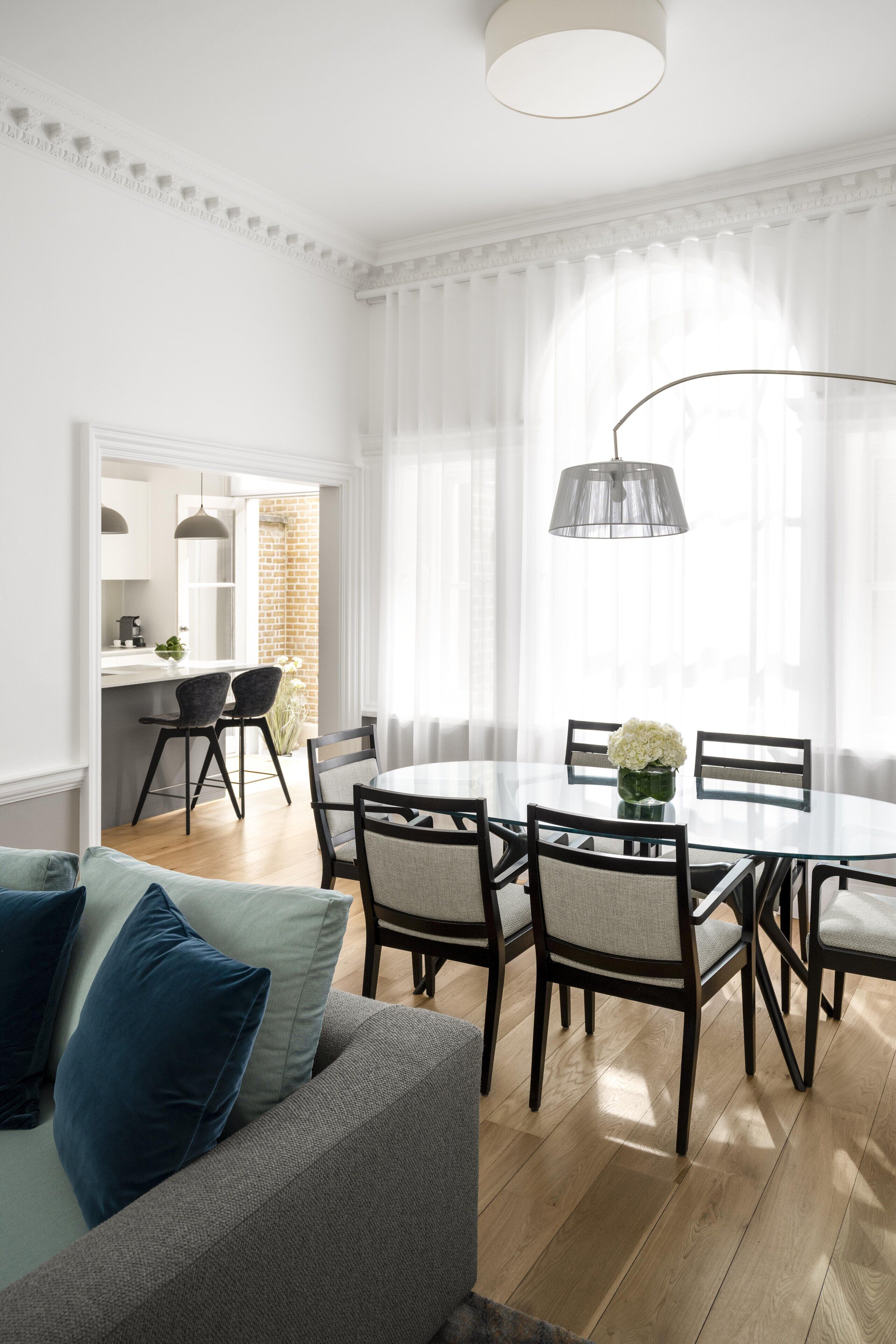 A modern dining area with a round glass table, black chairs, and a white dining set.