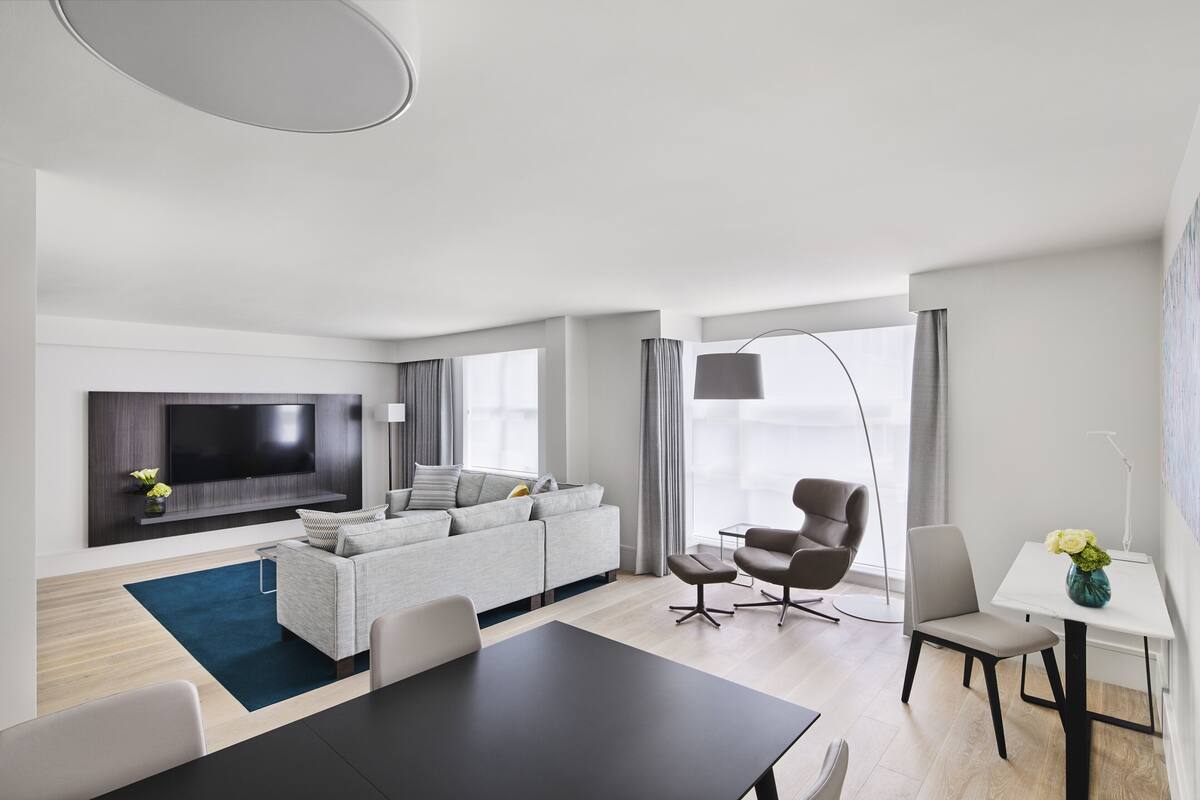 A modern living room with a flat-screen TV, grey sofa, dining table, and chairs.