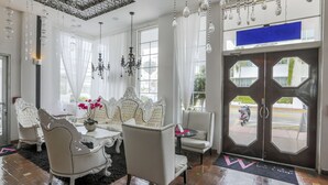 A hotel lobby with ornate white furniture, a chandelier, and a large door with a view of the street. - The Whitelaw Hotel (Miami Beach)