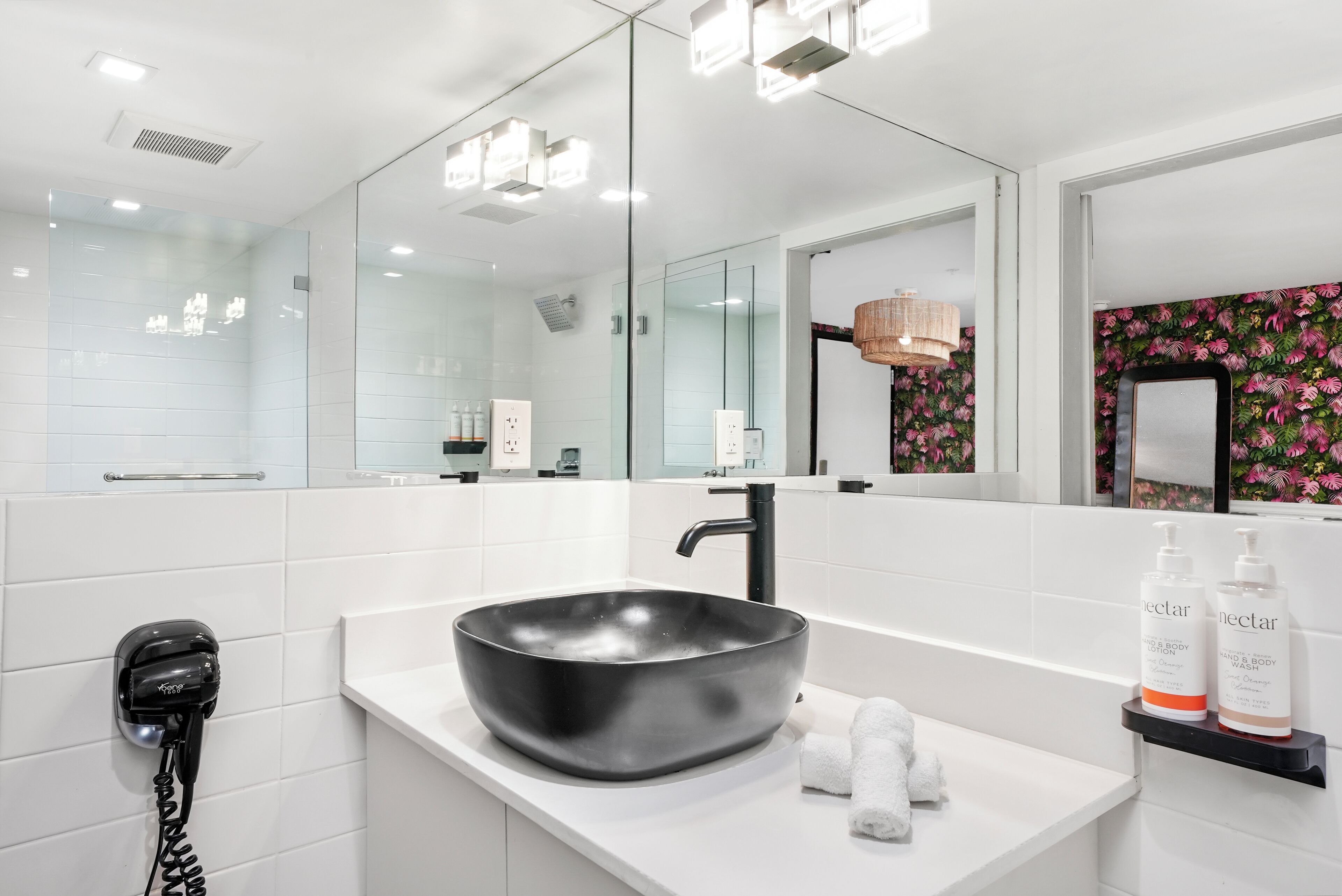 Ein modernes Badezimmer mit einem schwarzen Waschtischbecken, einem Handhaartrockner und einem Spiegel mit einem floralen Wandpapierbereich.