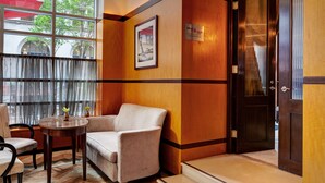 Un vestíbulo de hotel con un sofá, una mesita con jarrones, un cuadro en la pared y una puerta con un letrero.