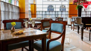 Un restaurante con mesas y sillas de madera, un jarrón con flores y vistas a la ciudad a través de amplios ventanales.
