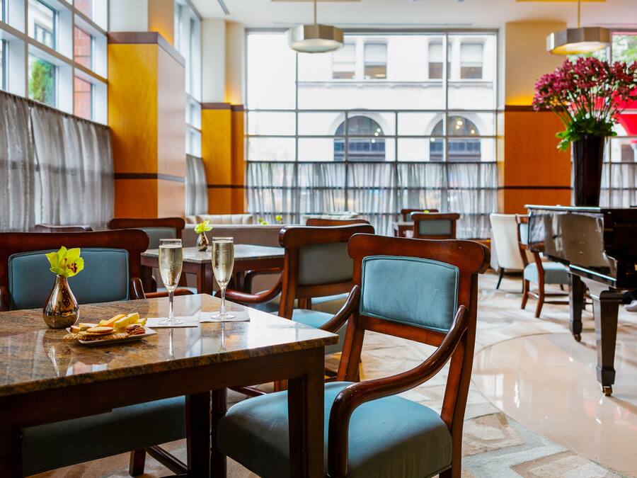 Un restaurante con mesas y sillas de madera, un jarrón con flores y vistas a la ciudad a través de amplios ventanales.