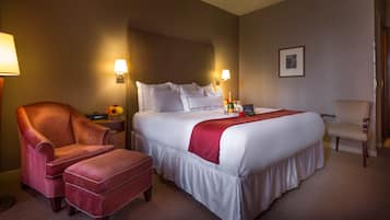 Habitación de hotel con una cama grande, dos sillones, una mesita de noche con lámpara y un cuadro en la pared.