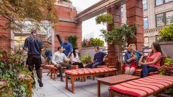 An outdoor seating area with wooden benches and tables, surrounded by brick walls and potted plants.
