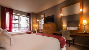 Habitación de hotel con dos camas, un escritorio, una silla, un televisor y un espejo grande.
