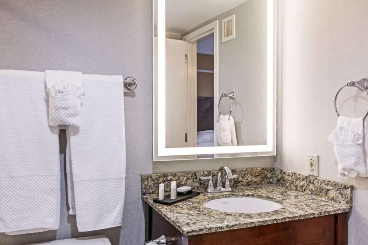 A bathroom with a granite countertop sink, a large mirror, and two white towels on towel racks.