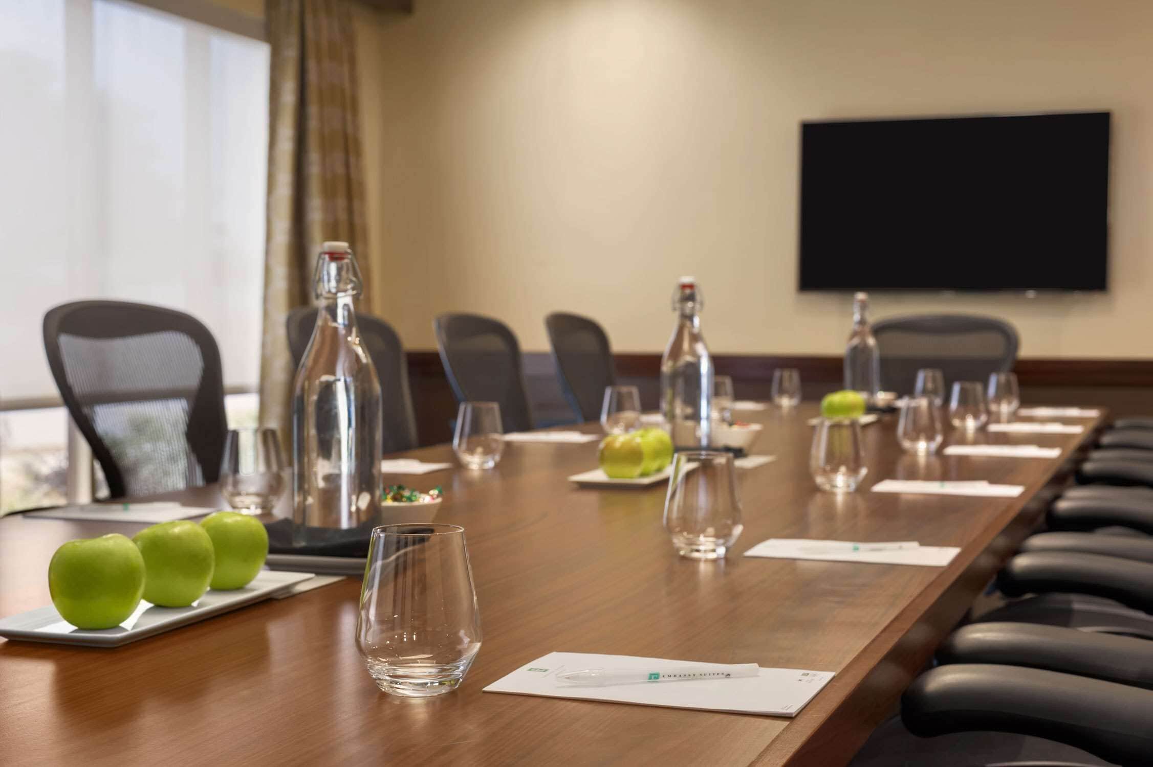 A conference room with a long table, chairs, and a television screen.