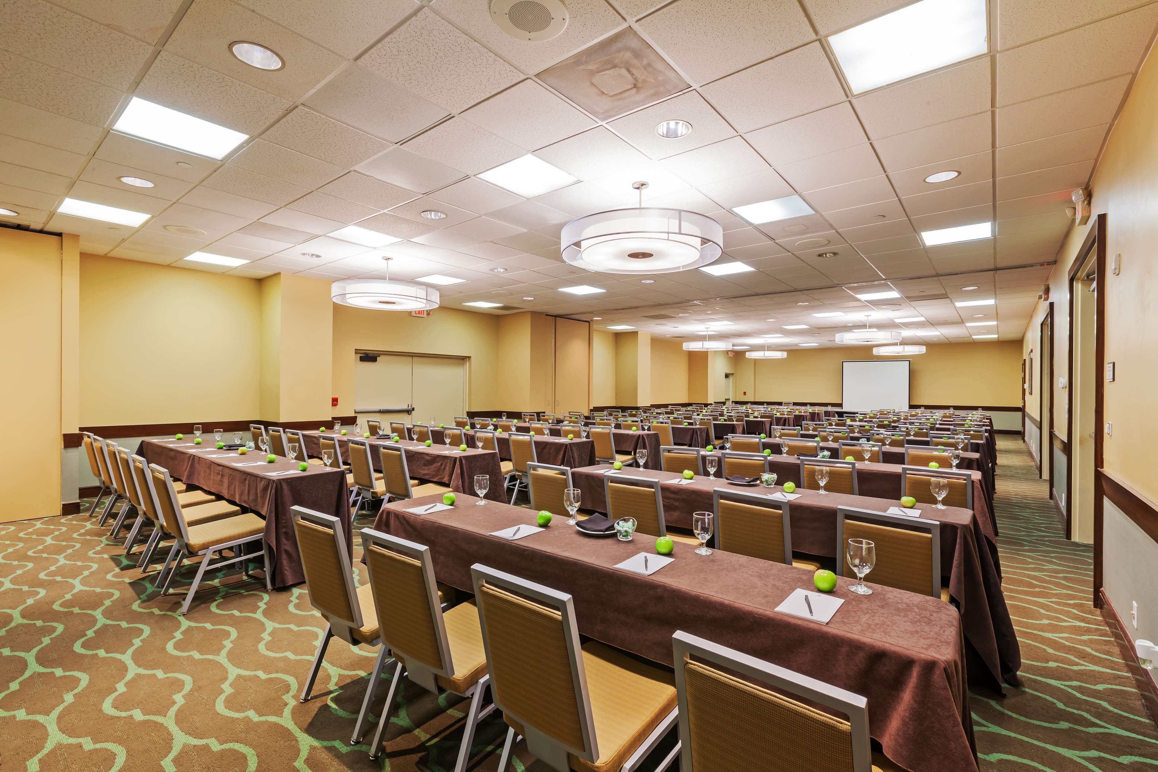 A conference room with rows of tables, chairs, and a projector screen.