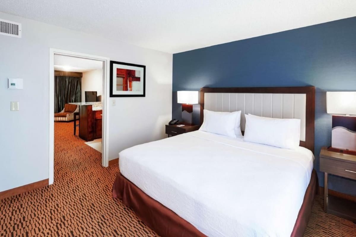 A hotel room with a large bed, bedside tables, a door leading to a bathroom, and a carpeted floor.