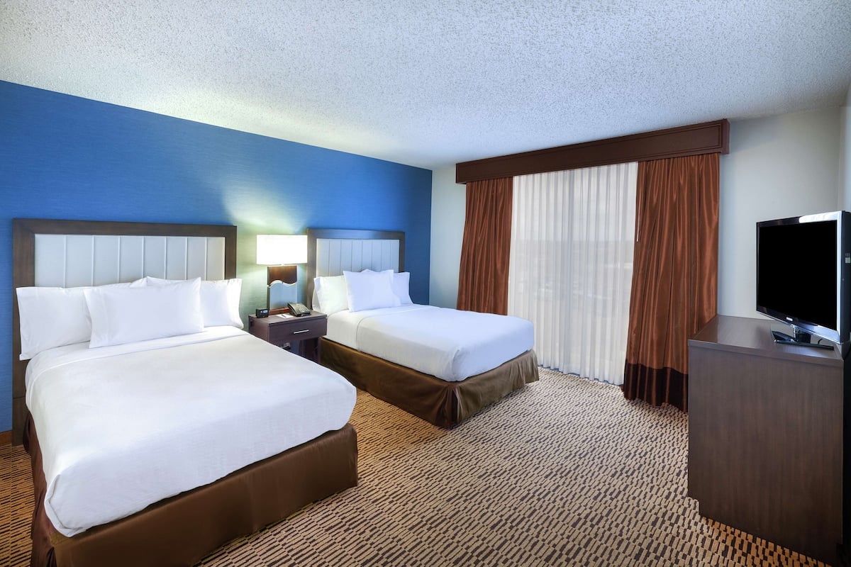A hotel room with two beds, a TV, and a desk.