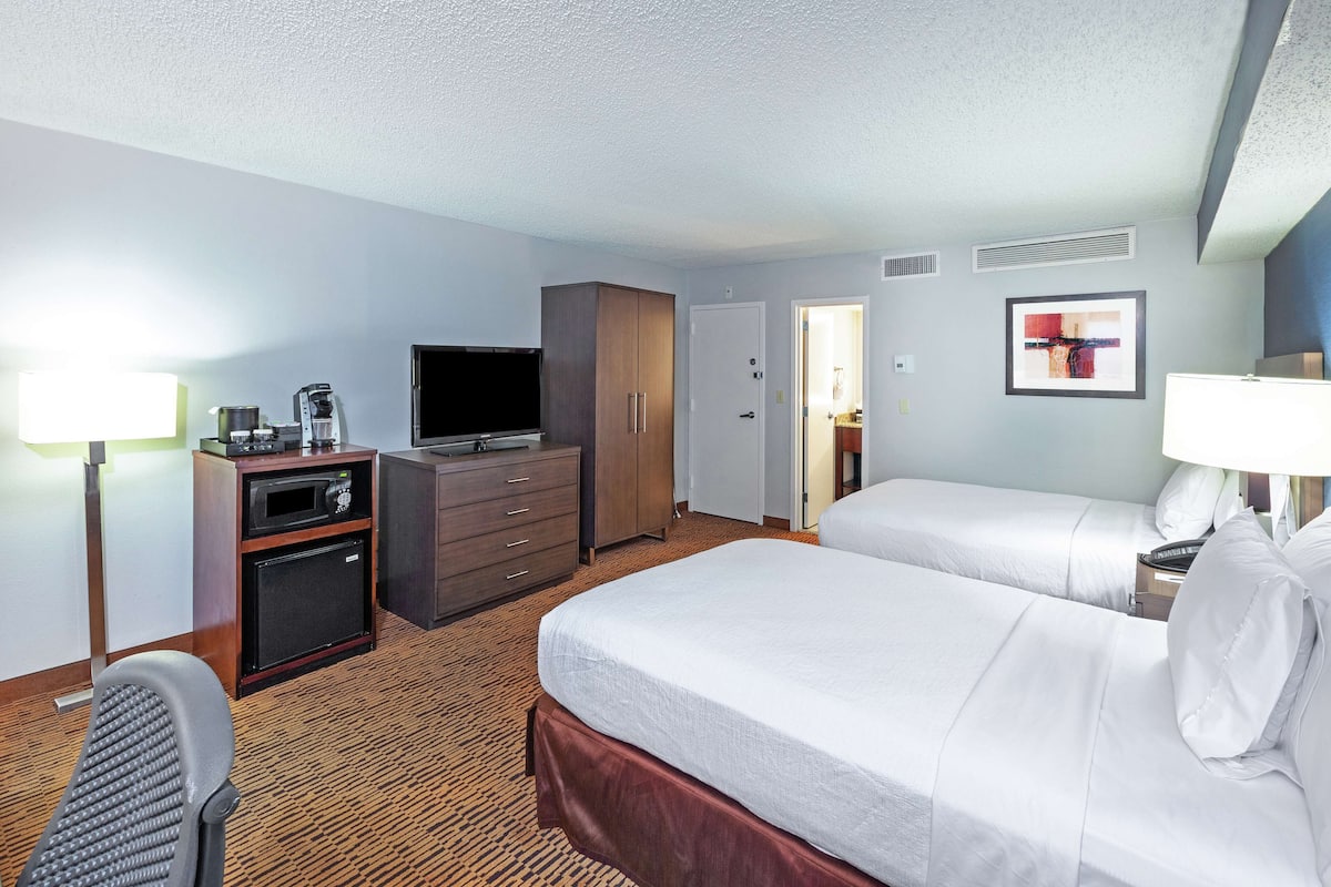 A hotel room with two beds, a TV, a desk with a lamp, and a microwave.