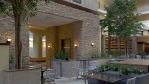 A spacious outdoor patio area with stone walls, multiple seating arrangements, and potted plants. - Embassy Suites by Hilton Dallas Market Center (Dallas)