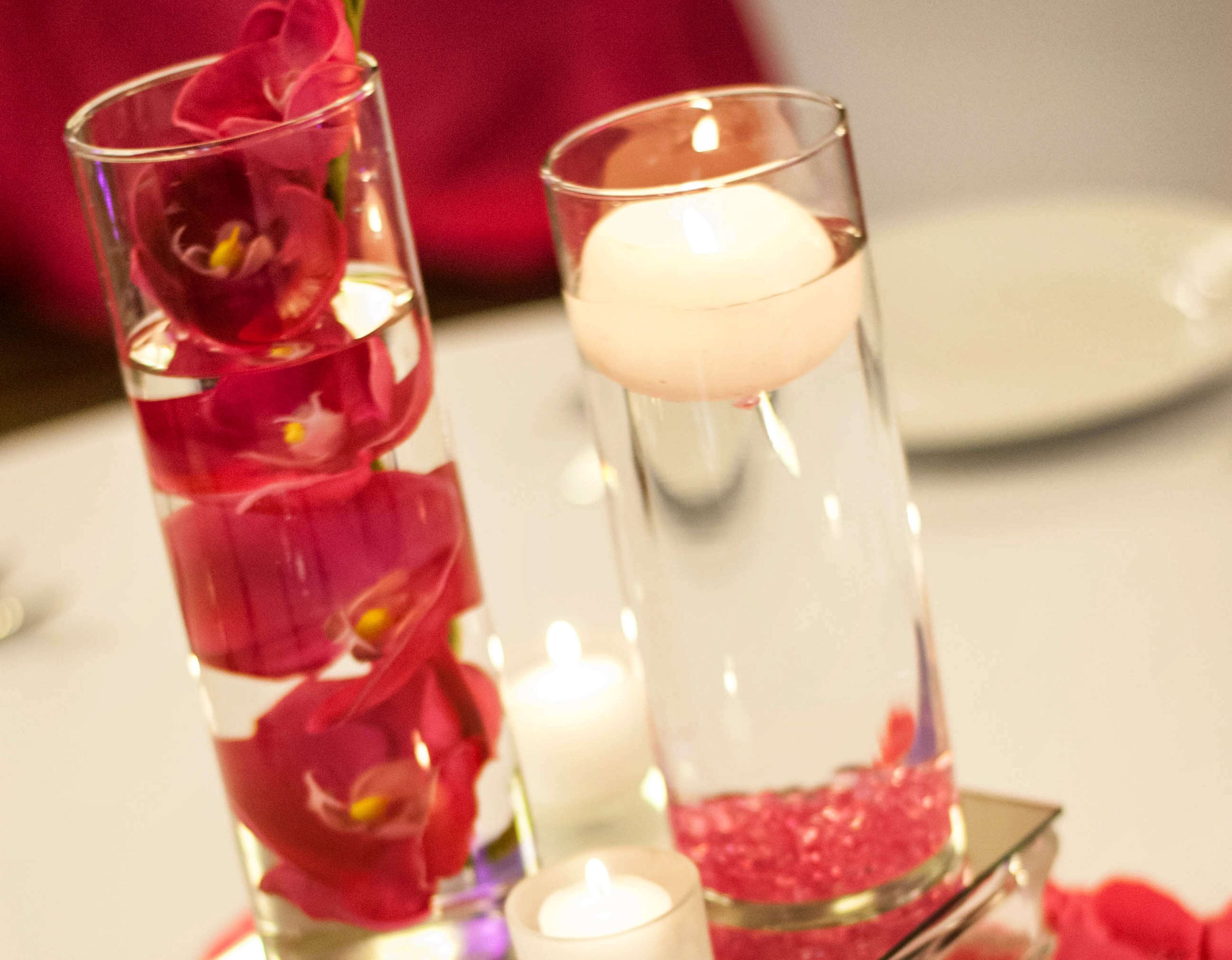 Deux vases en verre contenant de l’eau et des pétales de rose, ainsi qu’une bougie.