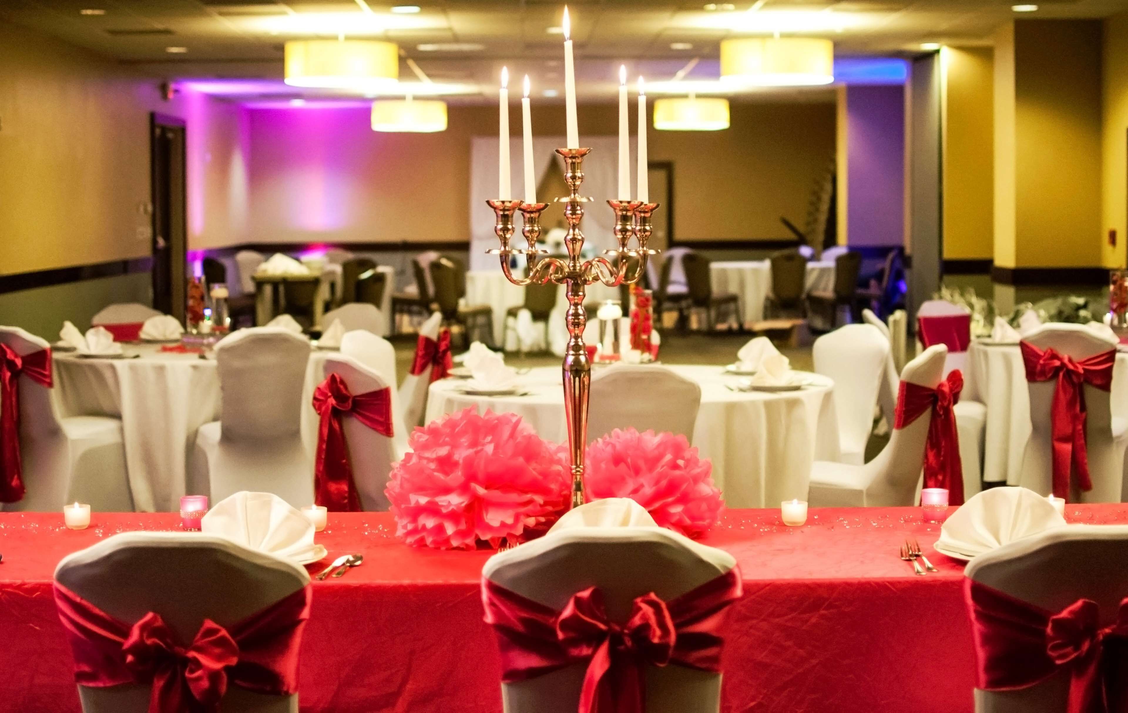 A banquet hall with round tables covered in white tablecloths, red sashes, and a central candelabra.