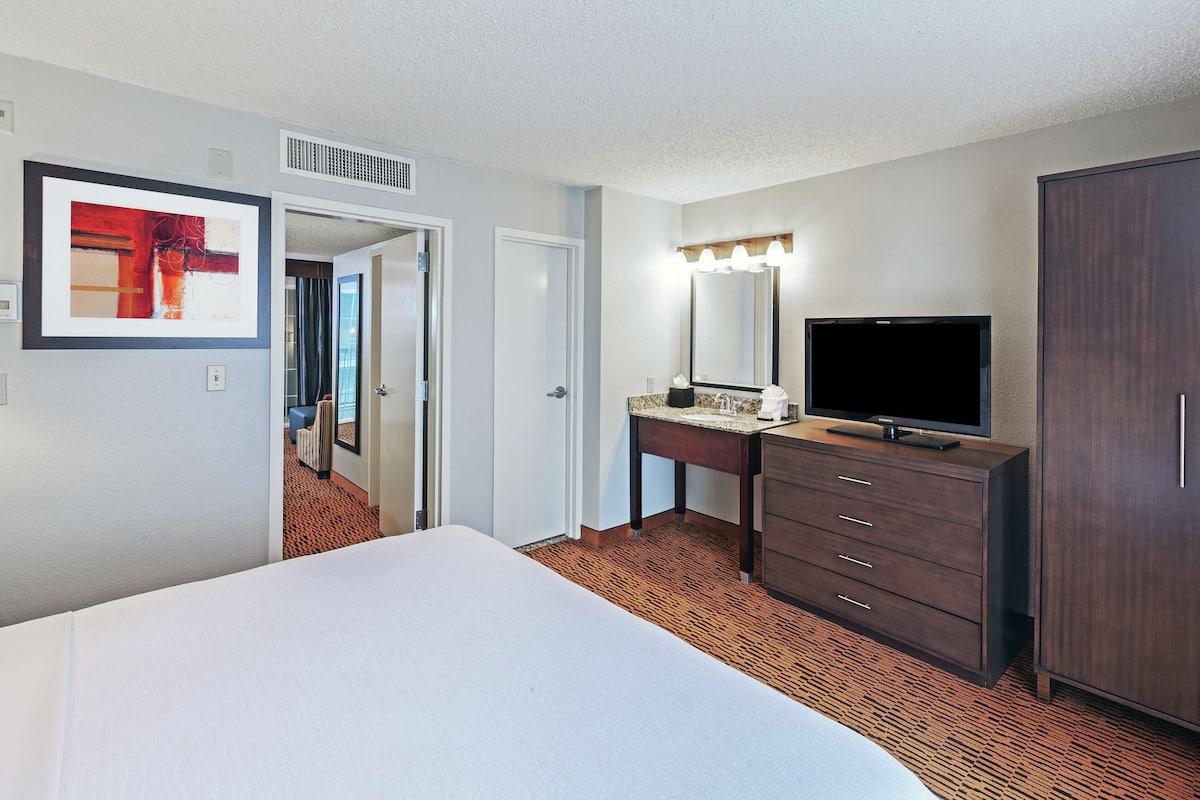 A hotel room with a large bed, a vanity with a mirror and lights, a television, and a wardrobe.