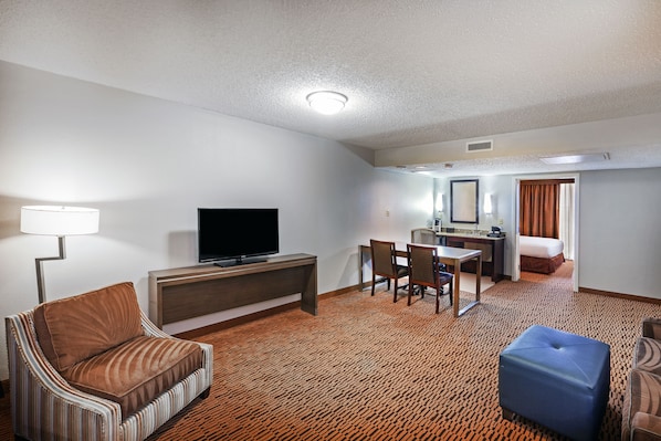 A hotel room with a TV, sofa, ottoman, dining table, chairs, and a bed.