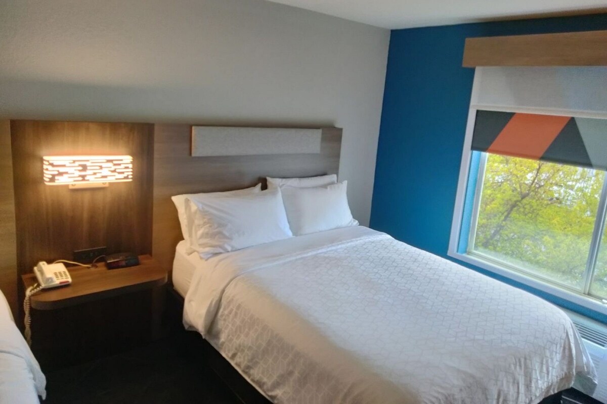 A hotel room with a bed, a bedside table with a phone, and a window with a view of trees.