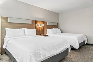 A hotel room with two beds, a wooden headboard, a wall-mounted light fixture, and a patterned carpet.