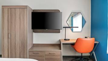 A modern hotel room with a wooden wardrobe, a flat-screen TV mounted on the wall, a desk with a chair, and a mirror.
