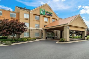 A Holiday Inn Express building with a covered entrance, multiple windows, and a landscaped area with trees and shrubs.