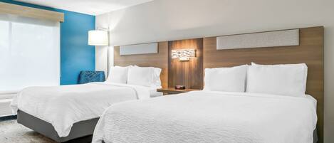 Habitación de hotel con dos camas, un ventanal grande, una lámpara de pared y un cabecero de madera.