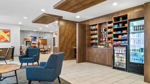 A modern hotel lobby with seating areas, a kitchenette, and a refrigerated beverage display. - Holiday Inn Express Lapeer by IHG (Lapeer)
