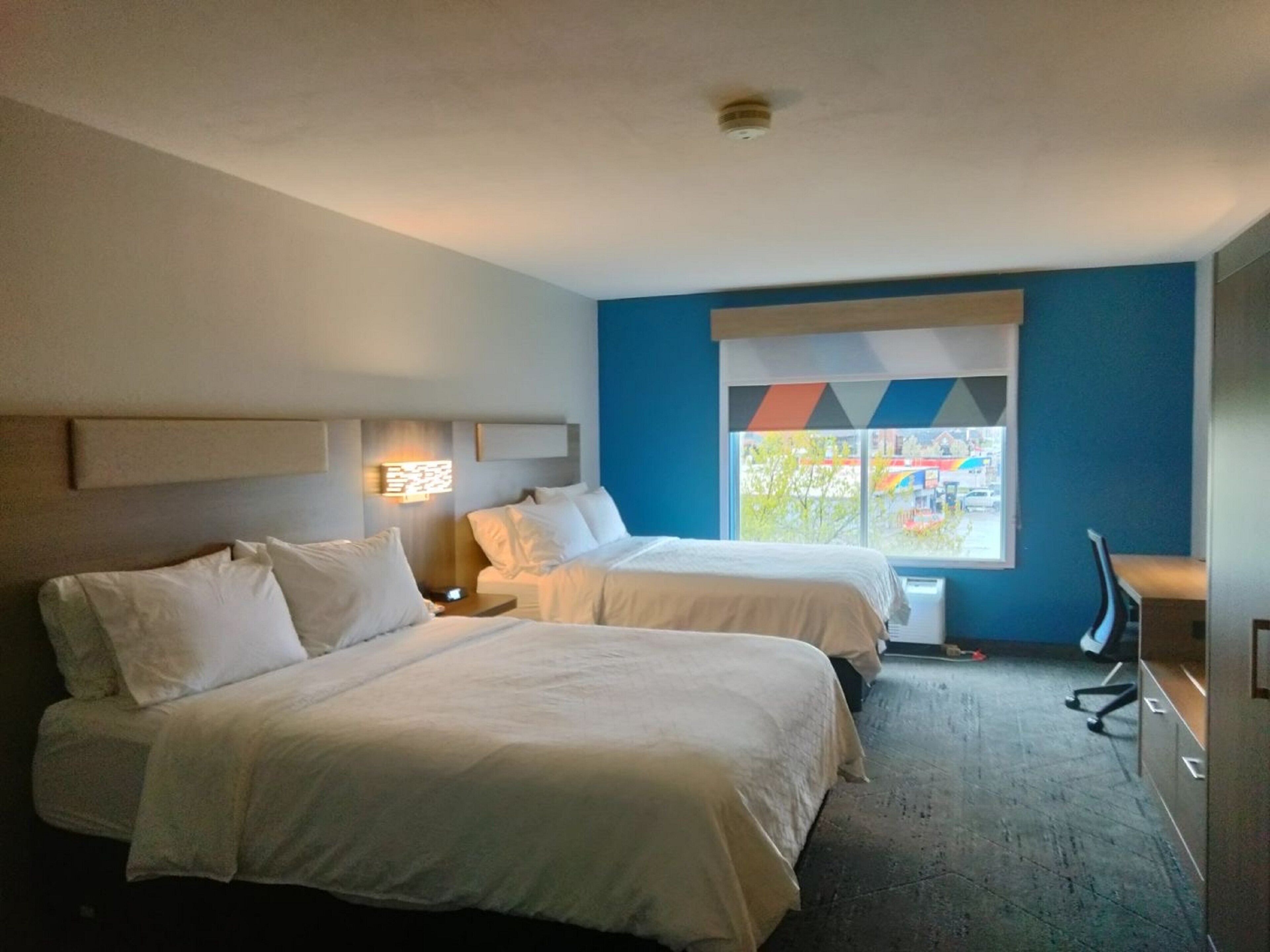 A hotel room with two beds, a desk, and a window with a view of the outside.