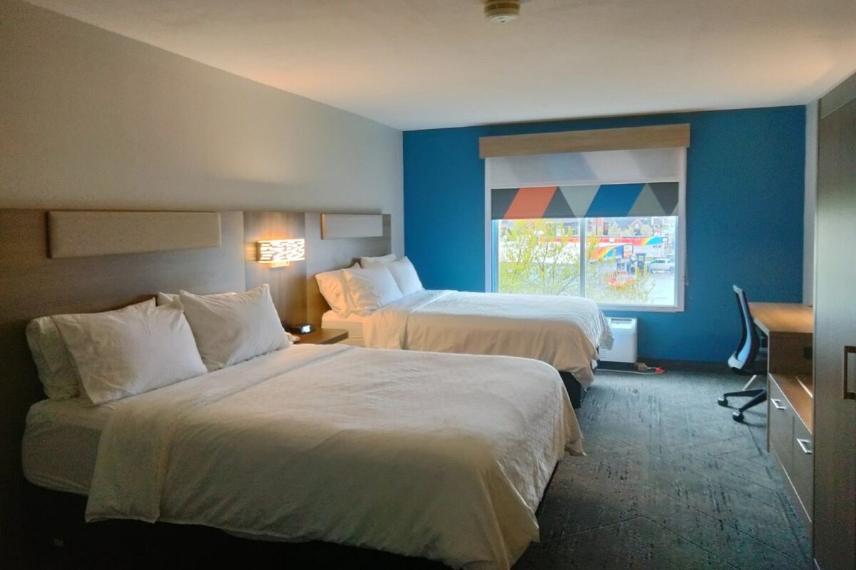 A hotel room with two beds, a desk, and a window with a view of the city.