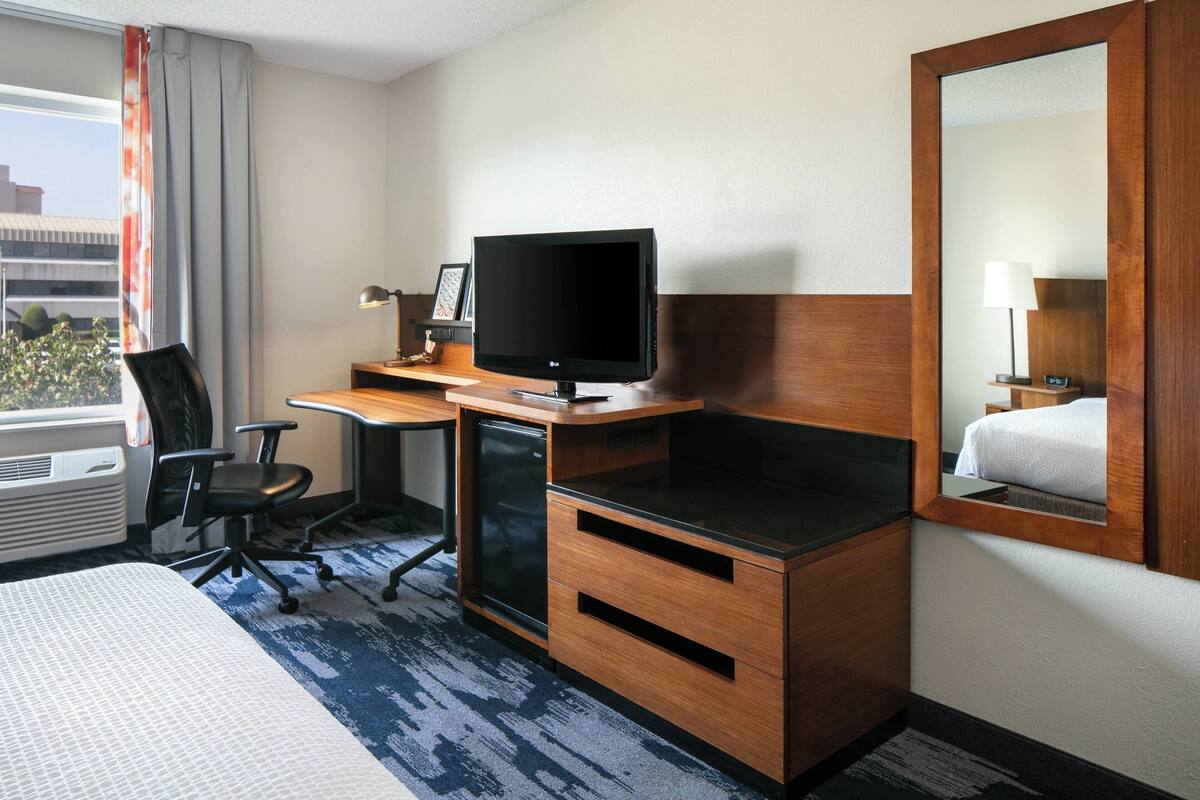 A hotel room with a bed, desk, television, and a mirror.