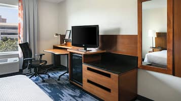 A hotel room with a bed, desk, television, and a mirror.