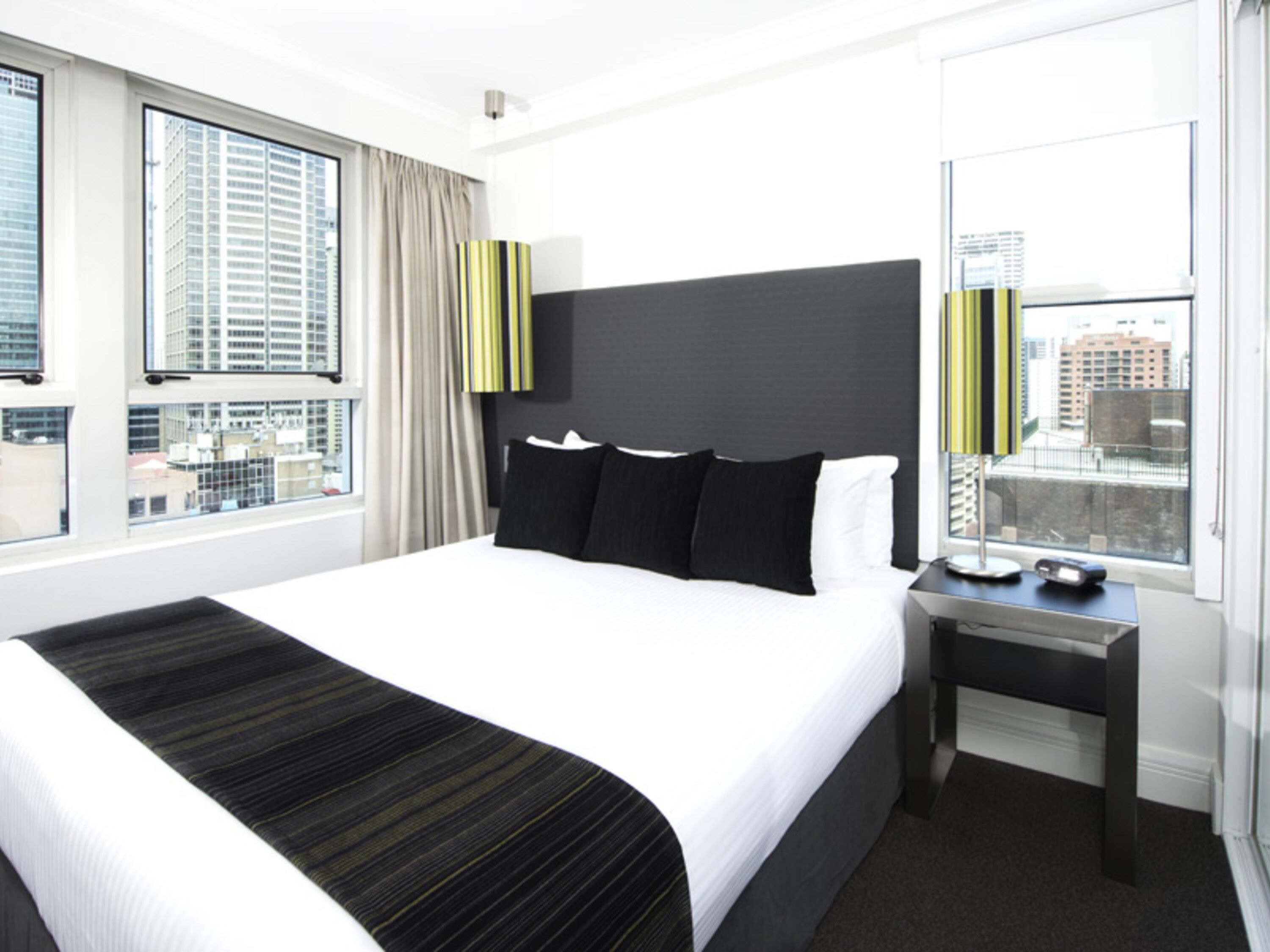 A hotel room with a large bed, a bedside table, a window with a city view, and a modern headboard.