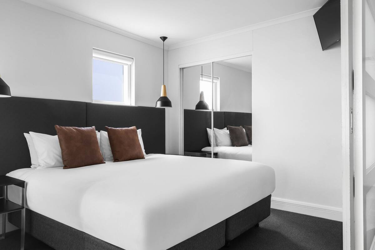 Una habitación de hotel moderna con una cama grande, una mesita de noche, un espejo y un televisor.