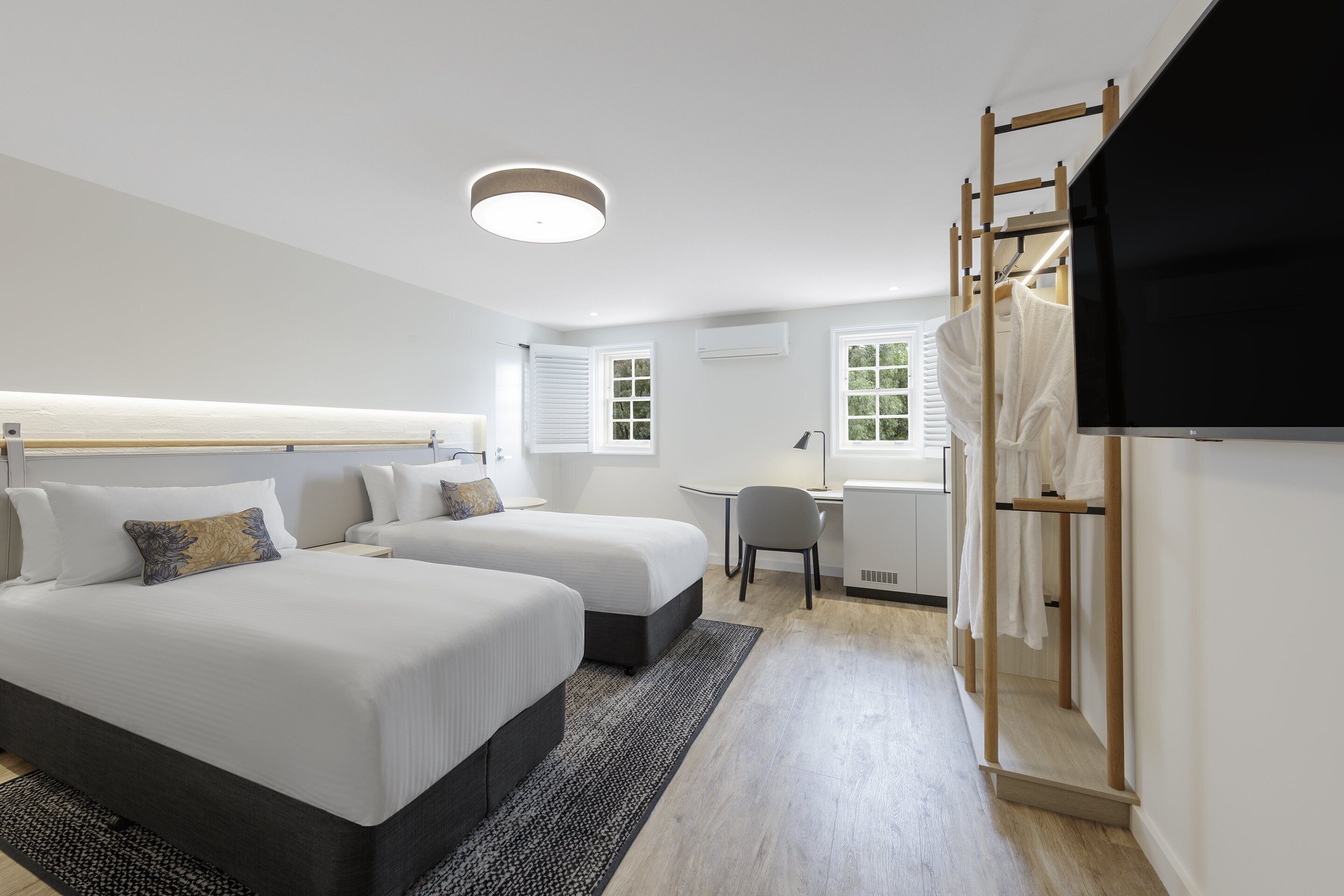 A modern hotel room with two beds, a desk, a chair, and a TV.
