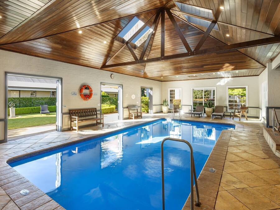 An indoor swimming pool with a wooden ceiling, clear glass doors leading outside, and a lifebuoy on the wall.